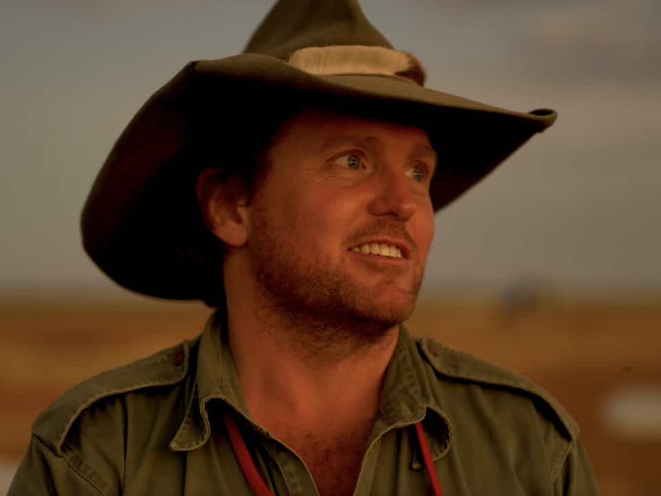 Close up of a man standing outside, wearing a hat