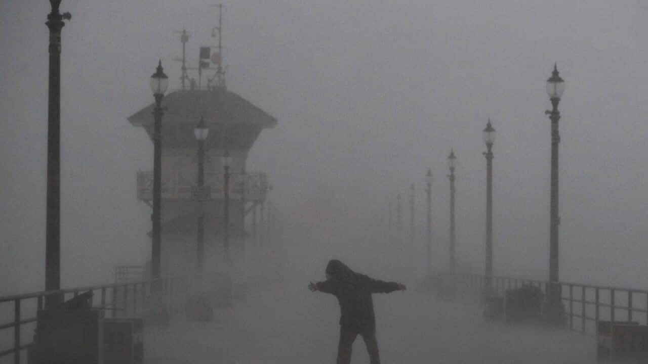 A man struggles against gusty wind and heavy rain in Huntington Beach