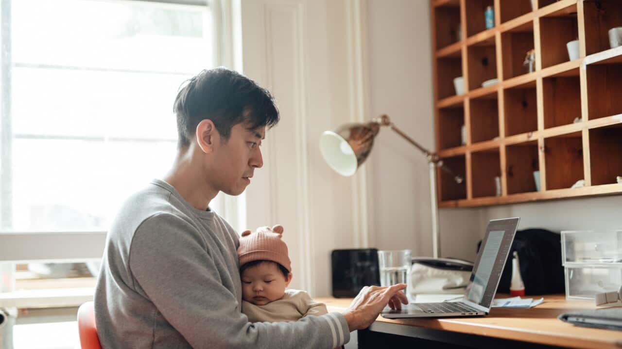 Young Asian father taking care of his baby while working from home with laptop