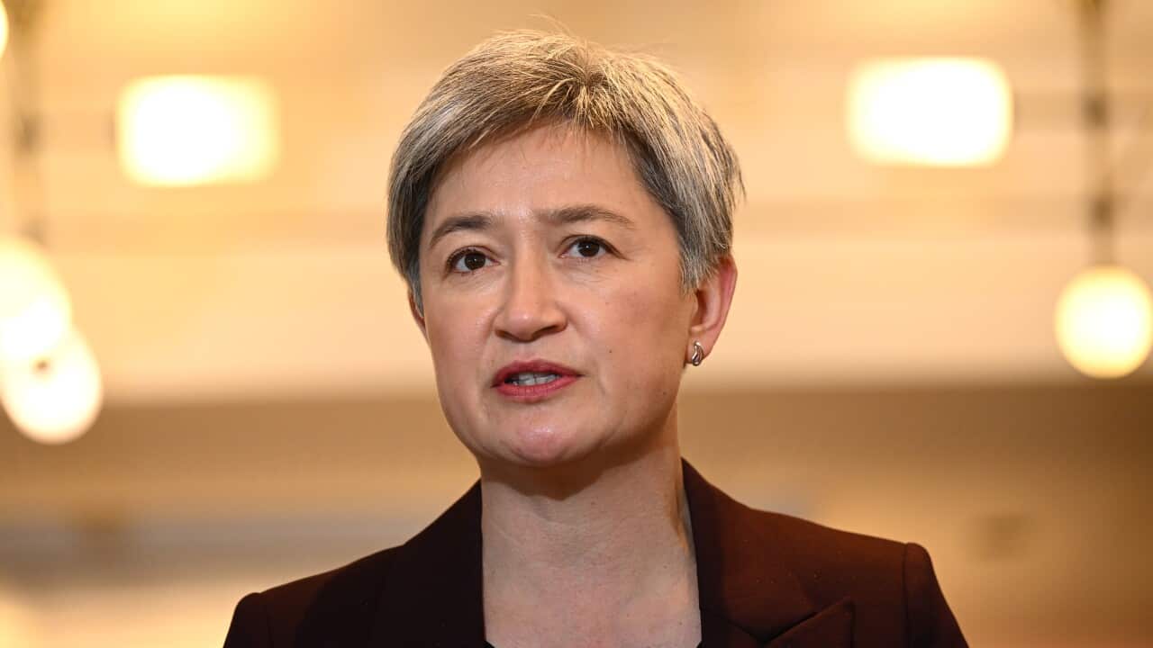A woman wearing a red coat speaks at a press conference.