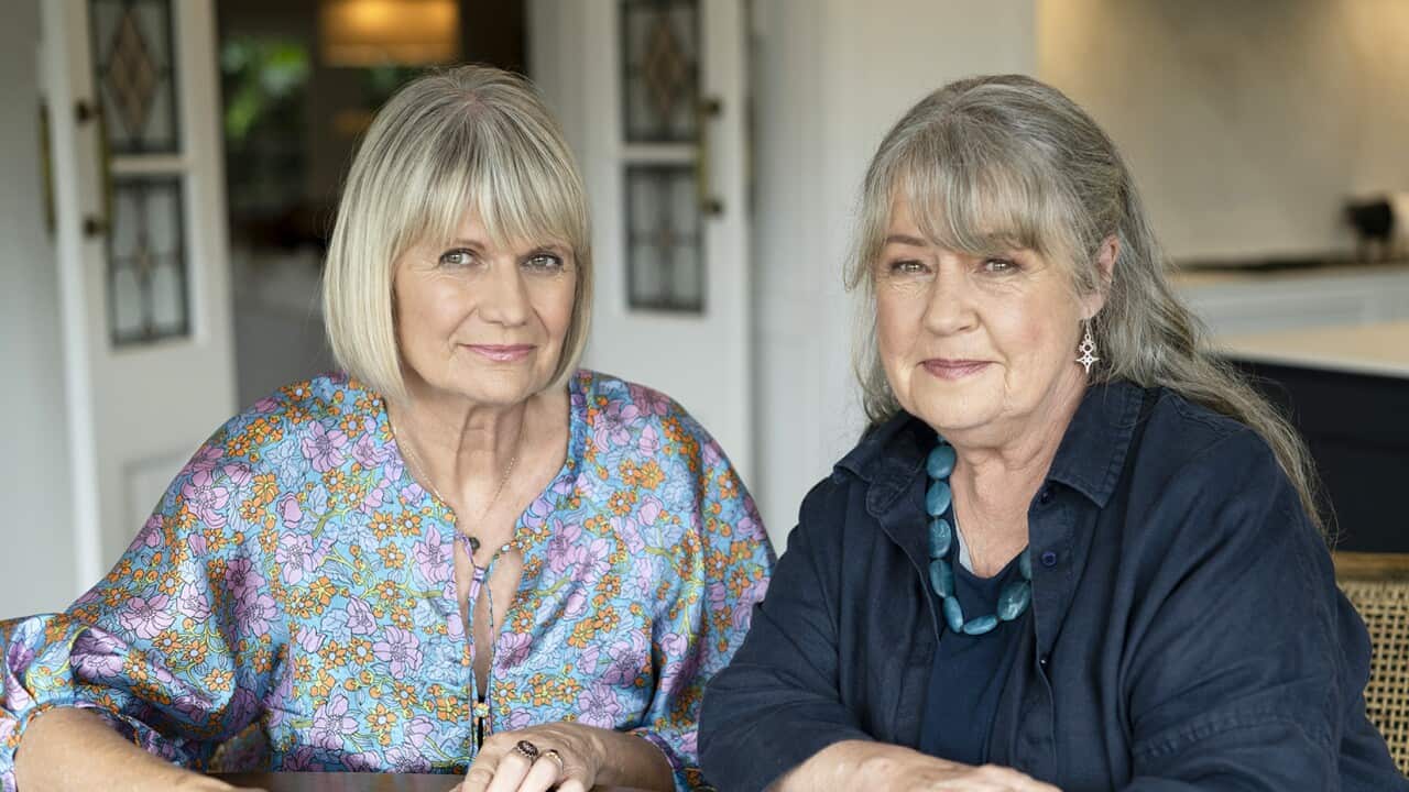 Two women sit at a table, on the table are several black and white photographs.
