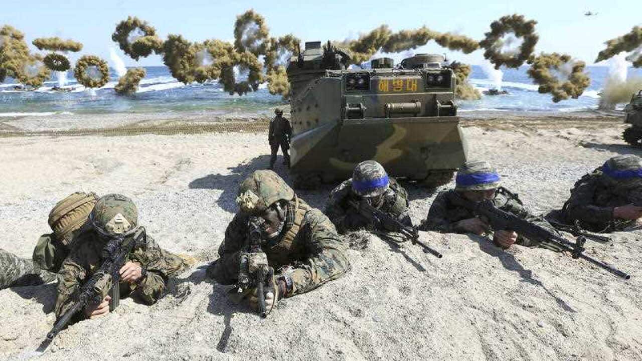 Marines of the U.S., left, and South Korea wearing blue headbands on their helmets, take positions after landing on a beach during the joint military combined amphibious exercise.