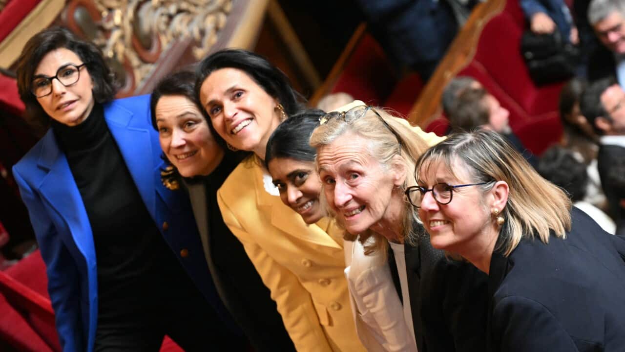 A row of six women in blazers of various colours smile for a photo