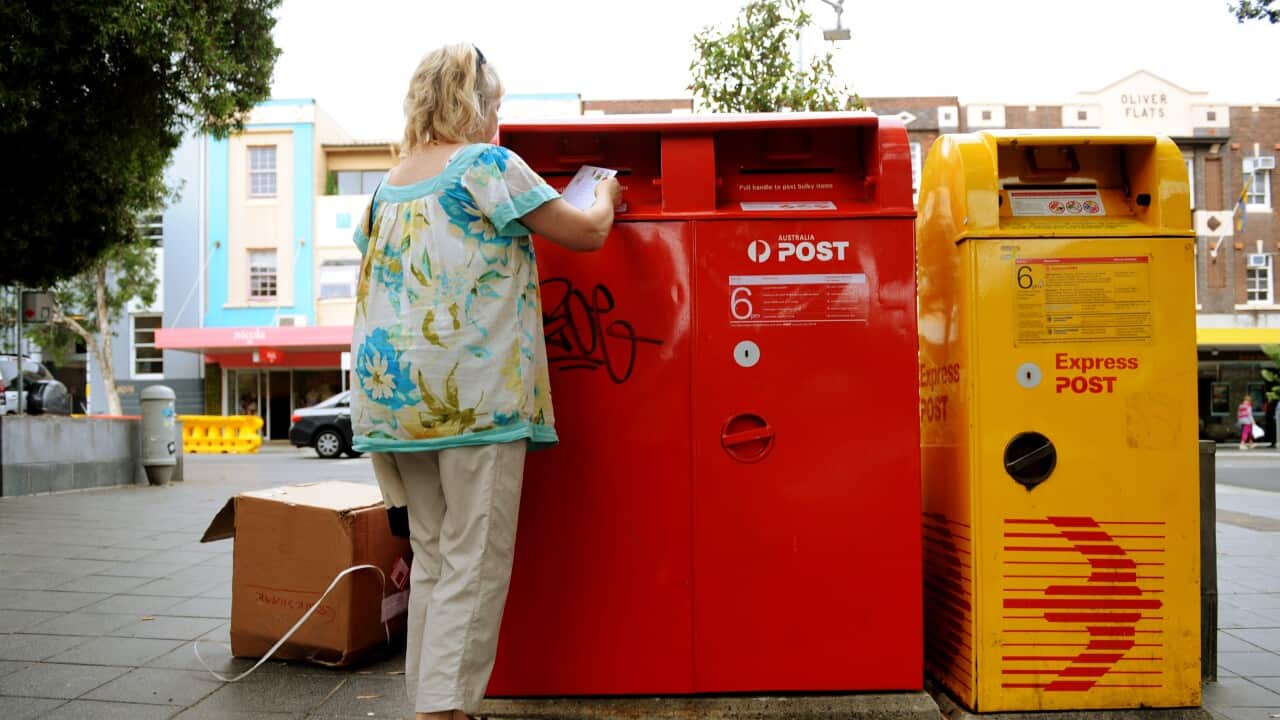 A woman putting a postal vote envelope inside of a red post box