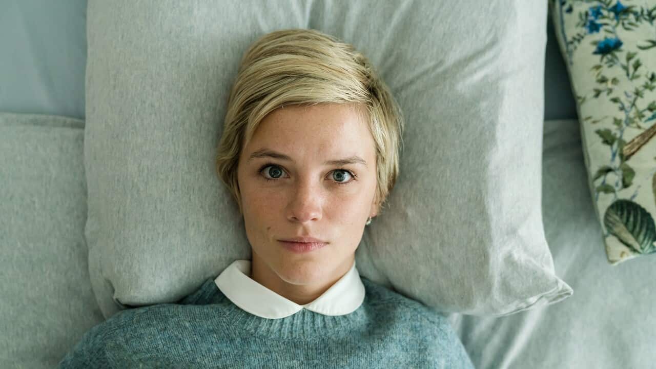 Seen from overhead, a young women lies in a bed, staring intently upwards.