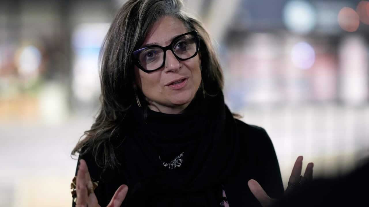 A woman with black glasses and a black top standing with hands up