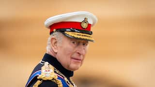 King Charles in formal royal attire, including a hat in red, white, black and gold.