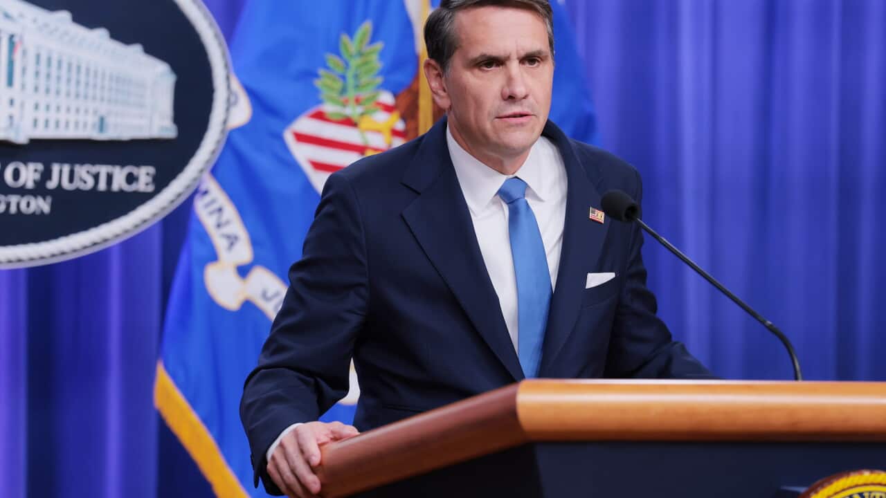 A middle-aged white man wearing a navy suit and tie speaking before a lectern
