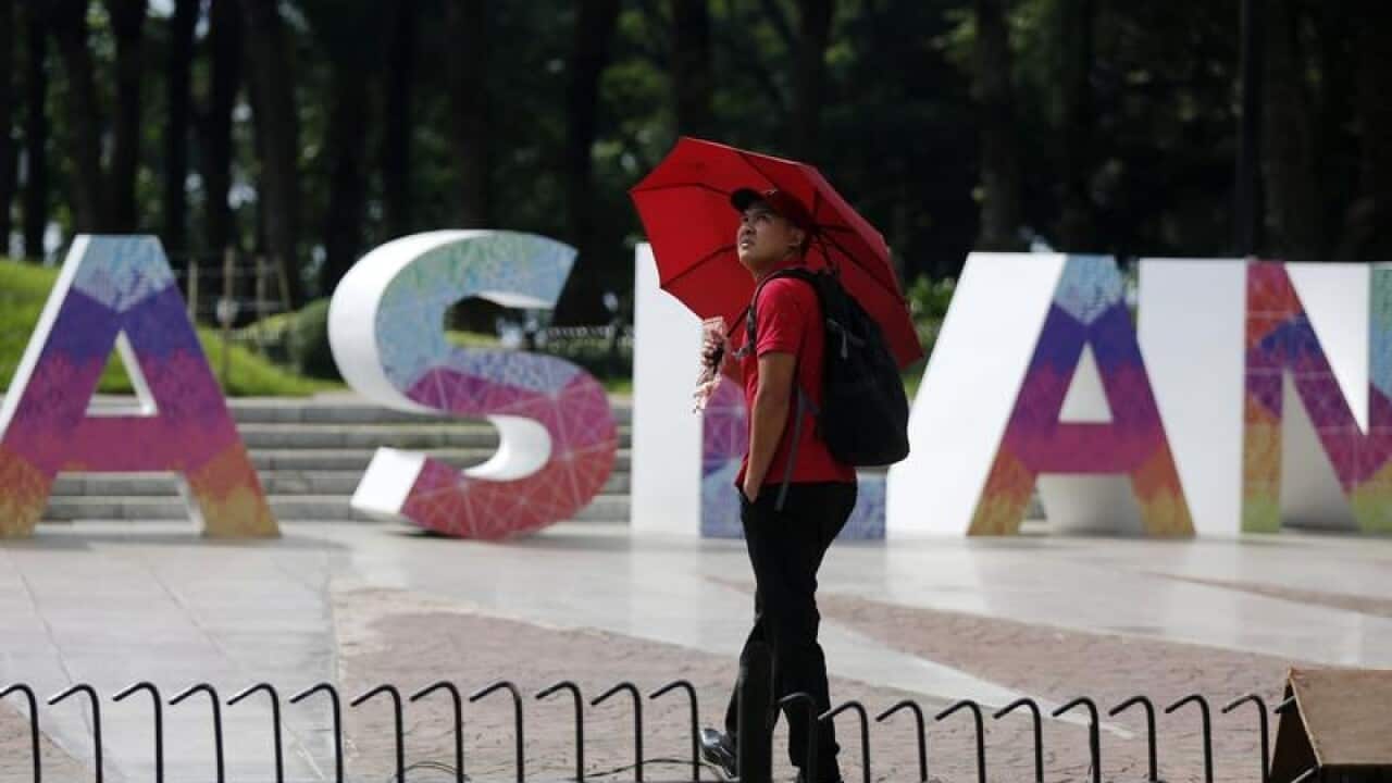 A man with an umbrella stands in front of an ASEAN logo in Manila.