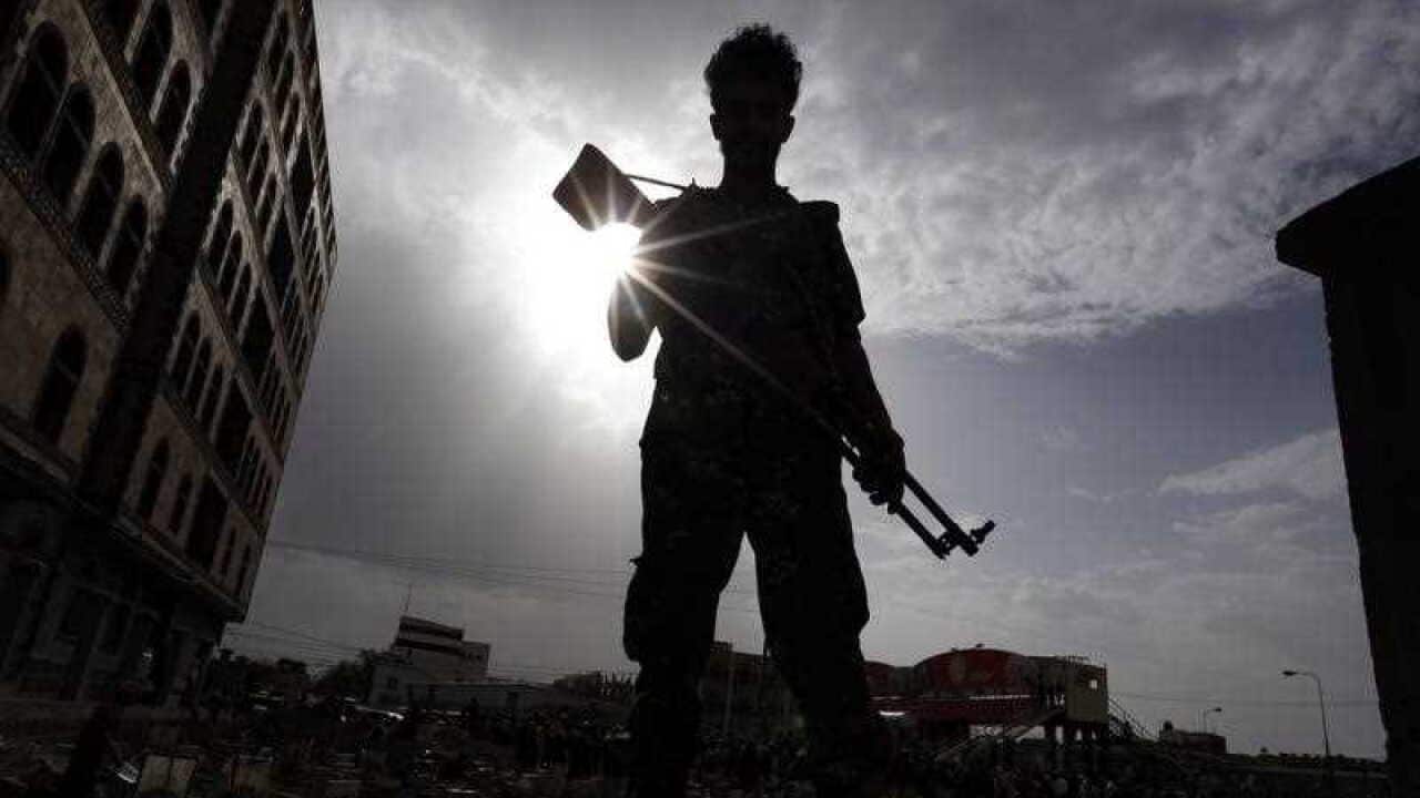 A Yemeni soldier stands guard as people bury the bodies of Houthi militia members allegedly killed during recent fighting at Yemen's western coast areas