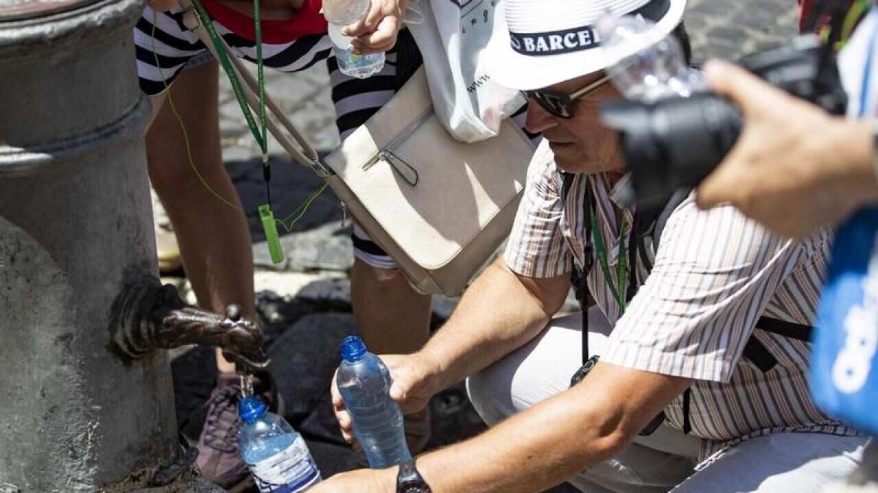 Tourists collect water to cool themselves at a fountain in Rome
