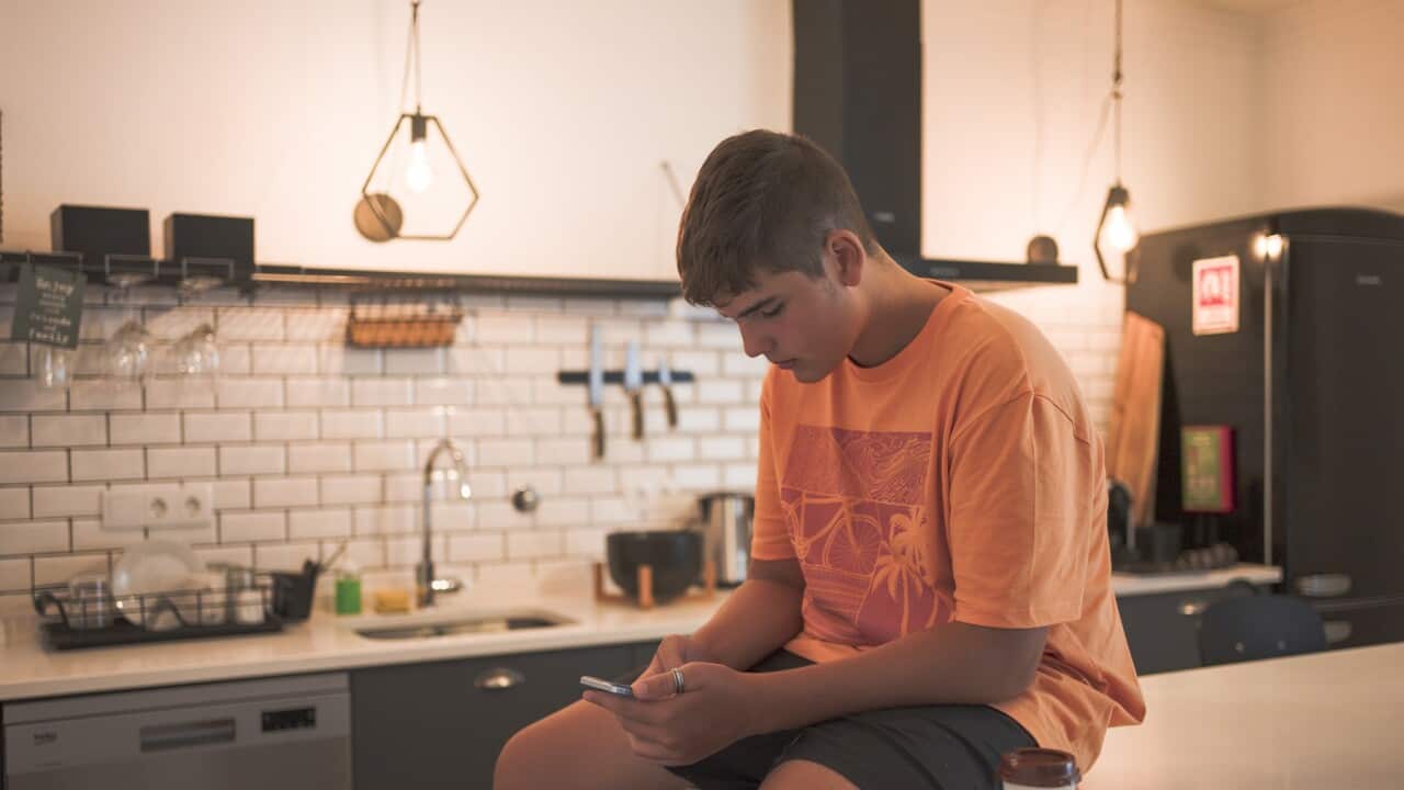 Teenage boy sitting at the kitchen table interacting with his smart phone while having a takeaway coffee