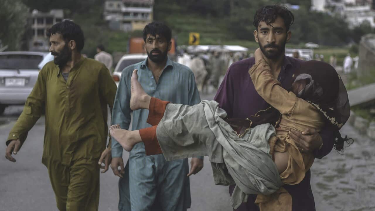 A man carries his sick daughter along a road damaged by flood waters