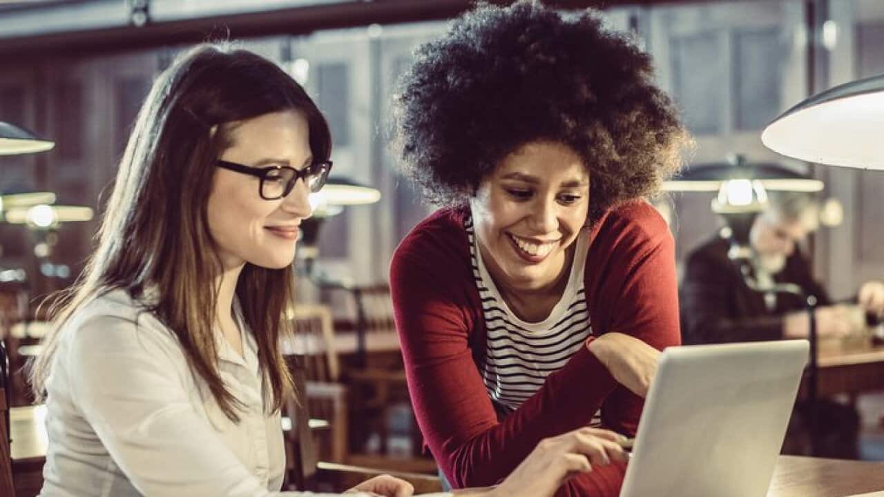 Two female students studying in the library and using laptop