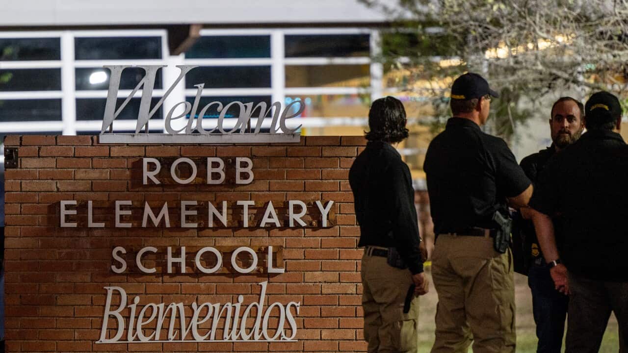 Law enforcement officers speak together next to Robb Elementary School sign.