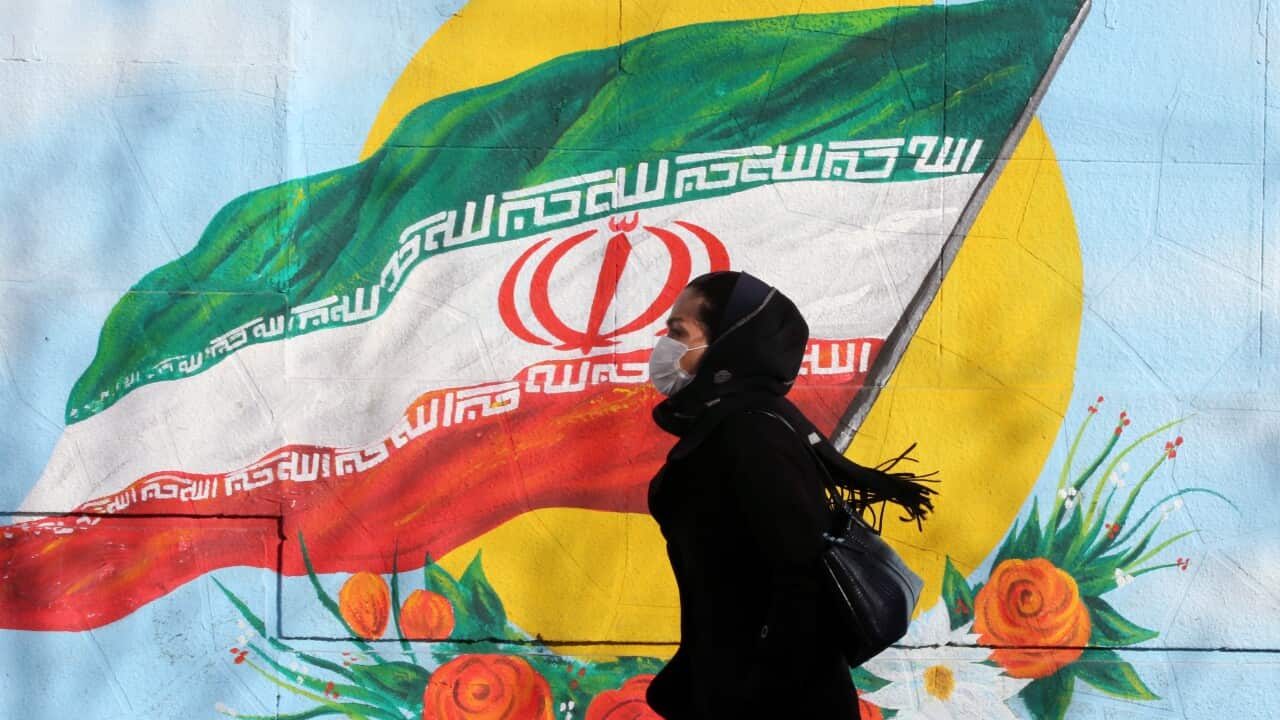 An Iranian woman wearing a mask walks next to a wall painting of Iranian national flag in Tehran, Iran.