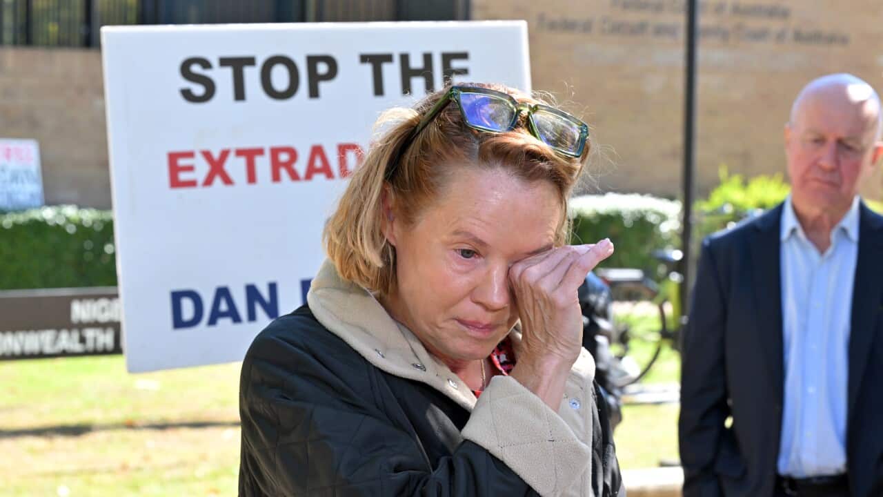 A woman in a black coat with white trim wipes her eyes, crying outside a court building