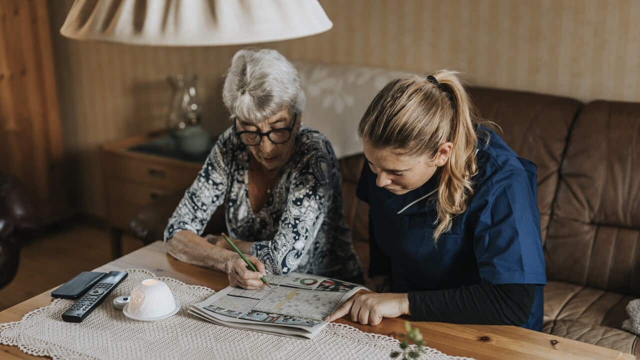 An old woman and a young woman sitting in a living room doing a crossword