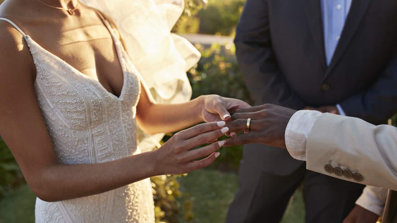 Midsection of a young bride exchanging wedding ring with groom while holding hands during the ceremony at sunset.