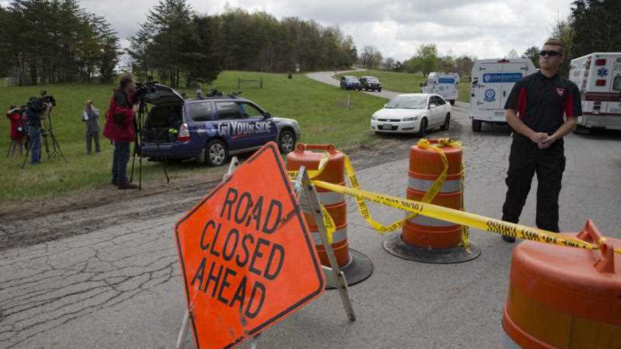 Media and emergency personnel stand at the perimeter of a crime scene as investigation vehicles arrive.