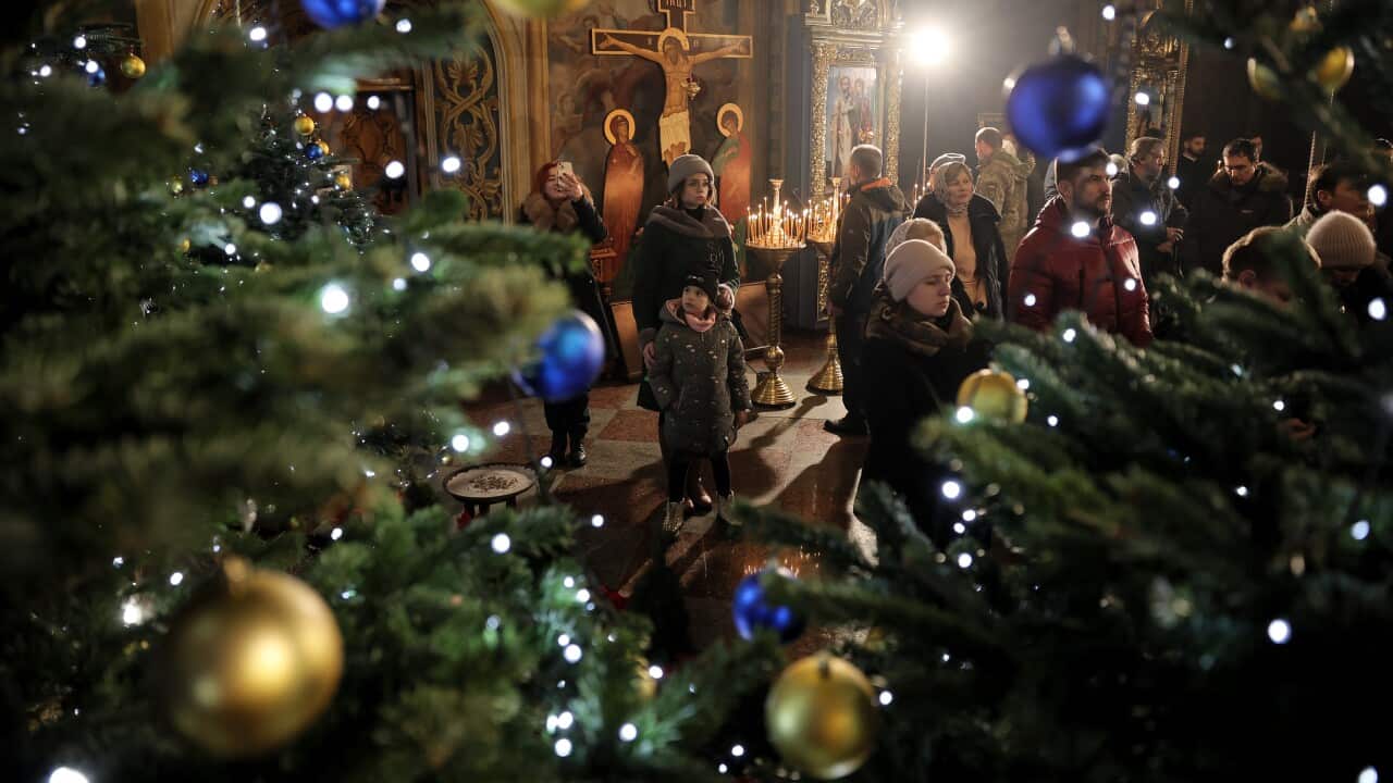 People stand next to a Christmas tree as they attend a Christmas Eve prayer service at the St. Michael's Golden-Domed Cathedral in Kyiv, Ukraine, 24 December 2023.
