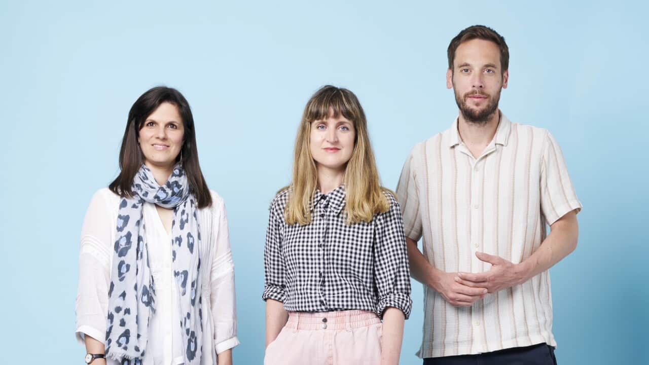A woman with dark hair and a scarf on the left. In the middle, a woman with blonde hair and pink trousers. Right, a bearded man in dark jeans.