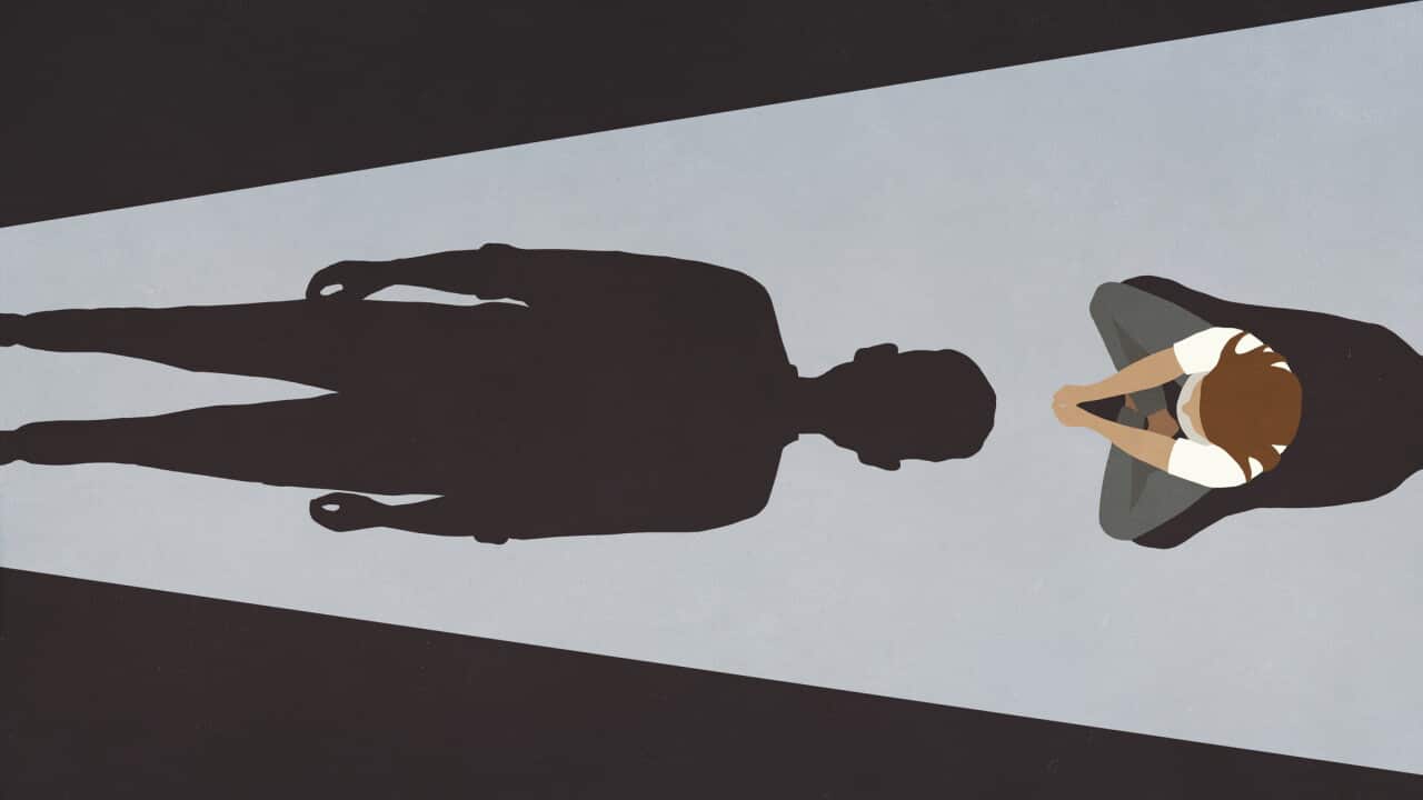 Woman sitting before looming male shadow