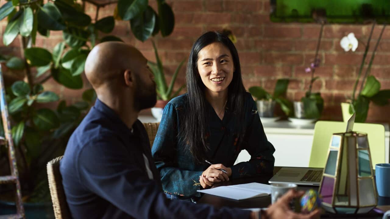 Mid adult Asian woman smiling towards male colleague
