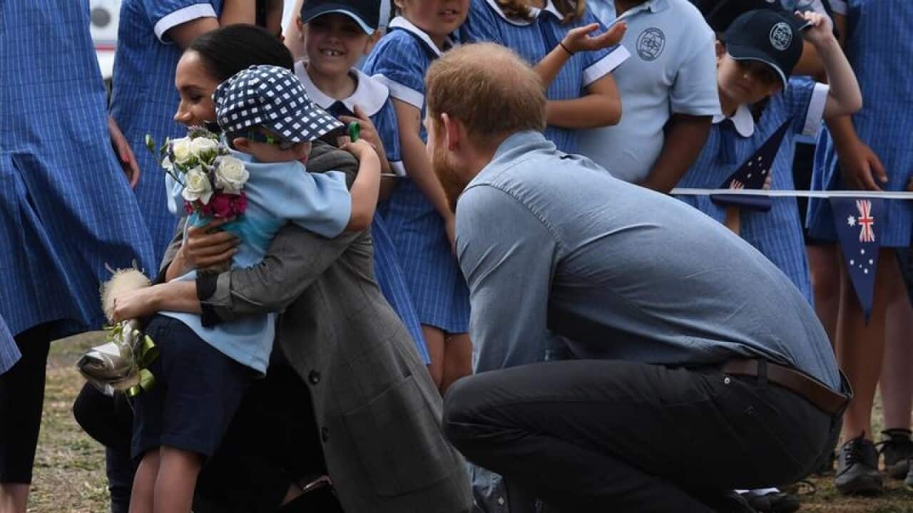 Meghan hugs five-year-old Luke Vincent while Prince Harry watches on.