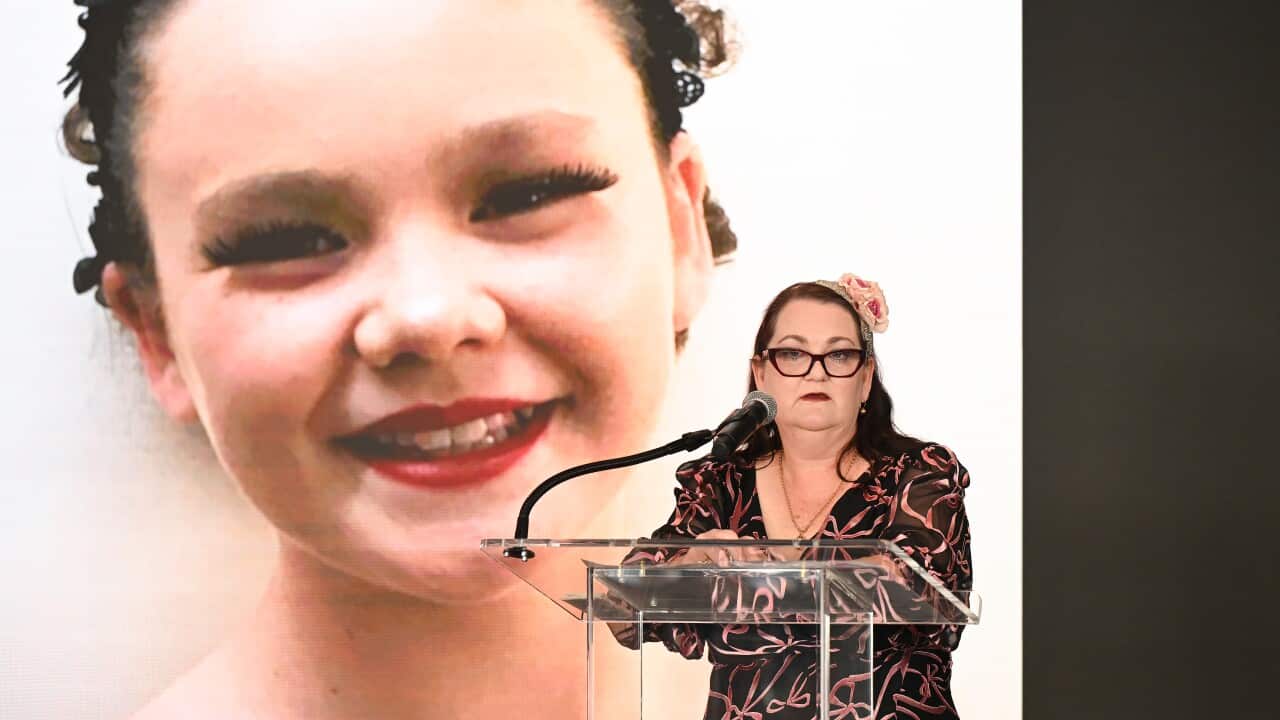 A women speaks at a lectern in front of a photo of a young girl