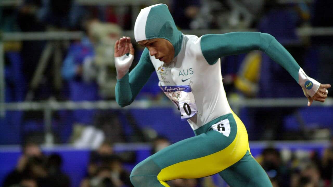 A woman in a green, gold and white track suit runs.