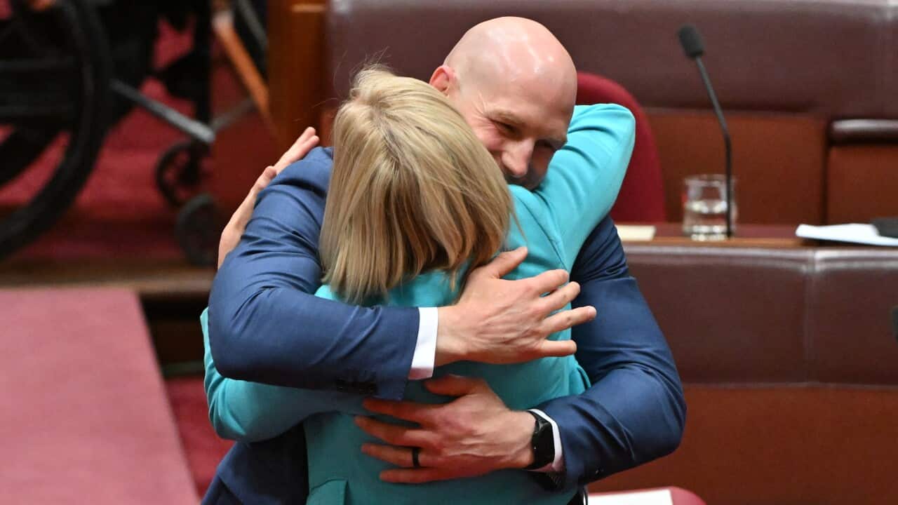 A bald man hugs a blonde woman in the Senate chamber