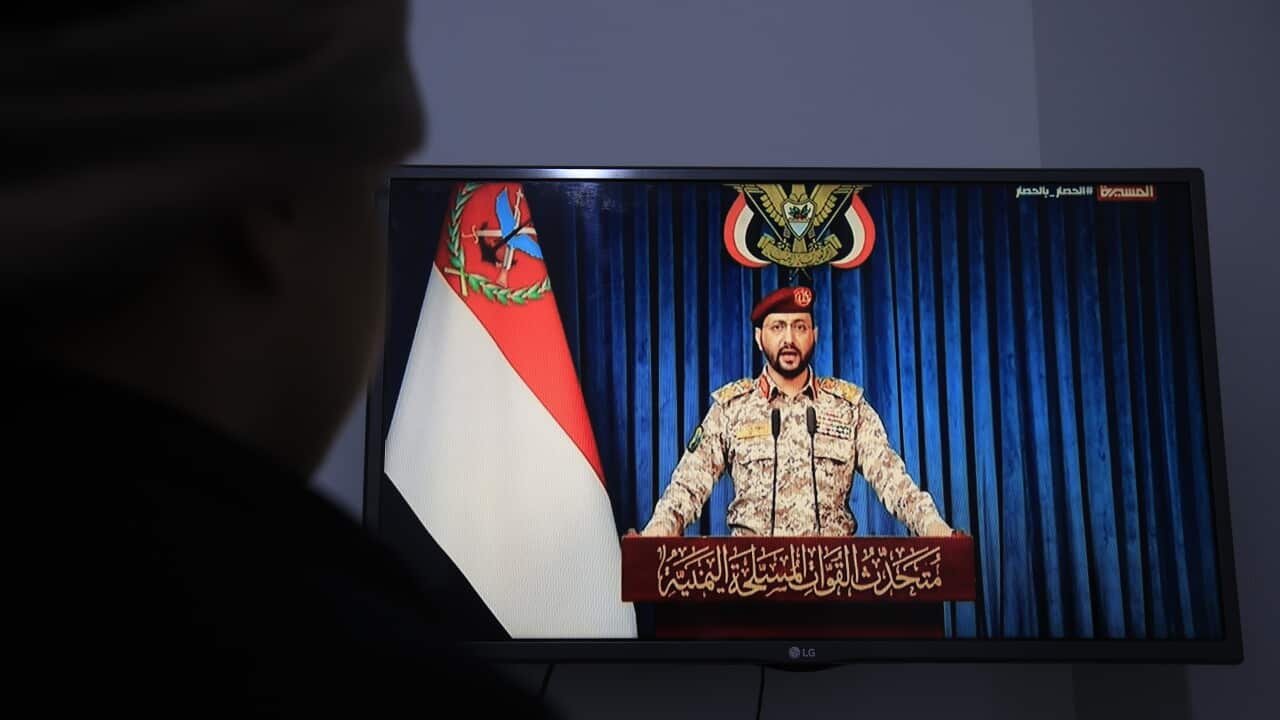 A person watches a TV screen that is showing a man in military uniform