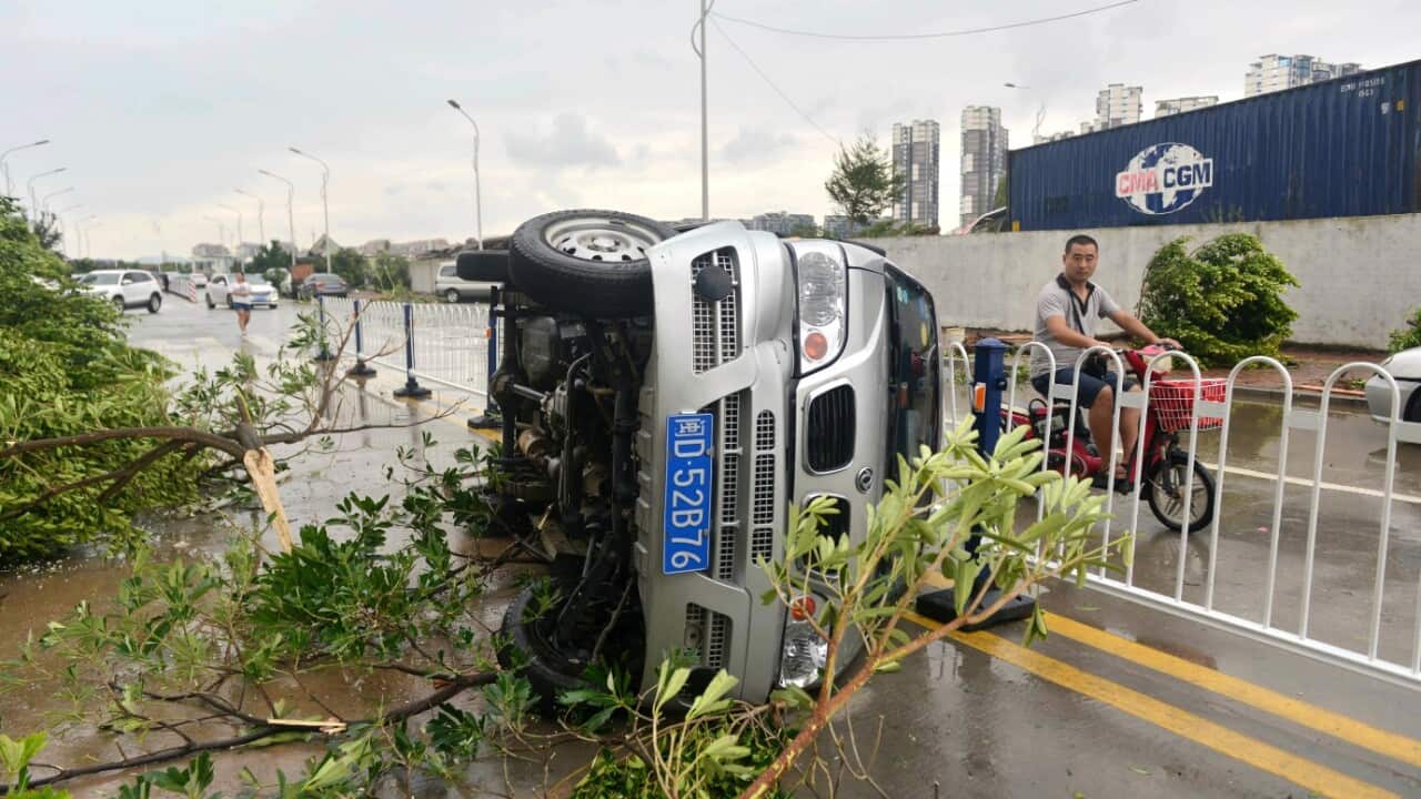 A man rides a scooter past an overturned vehicle and fallen trees after a typhoon in Xiamen in southeastern China's Fujian province Thursday, Sept. 15,