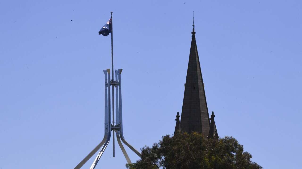 The spire of St Andrews Presbyterian Church near the flag pole of Australian Parliament House in Canberra