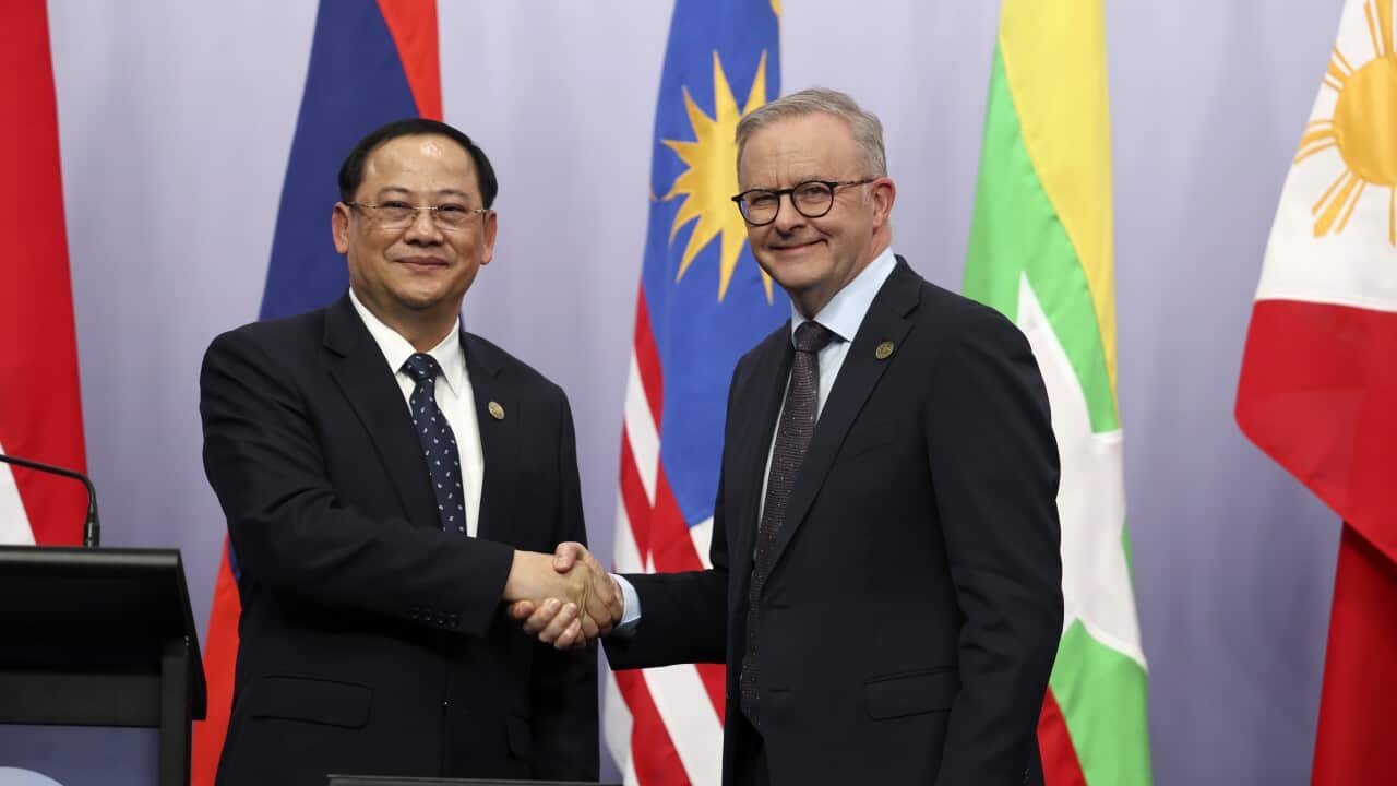 Two men in black suits shake hands in front of colourful flags