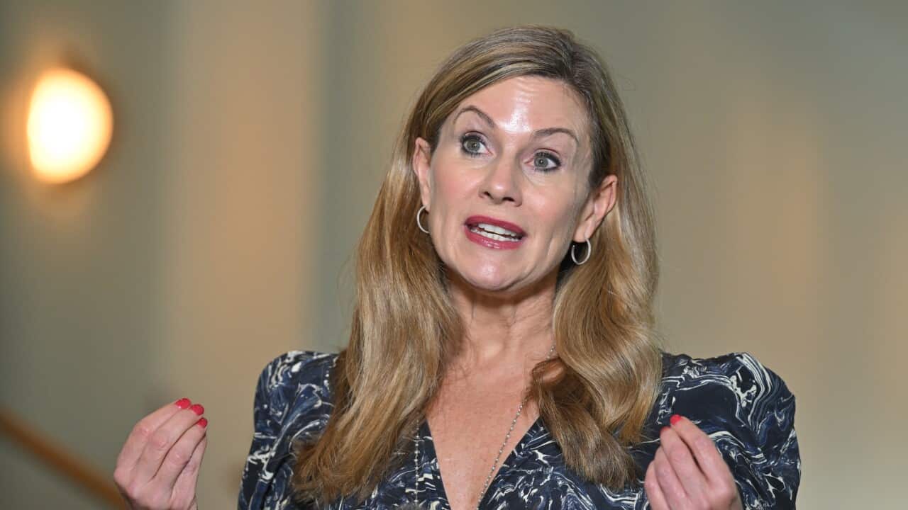 A woman with blonde hair in a black and white dress, gesticulating.