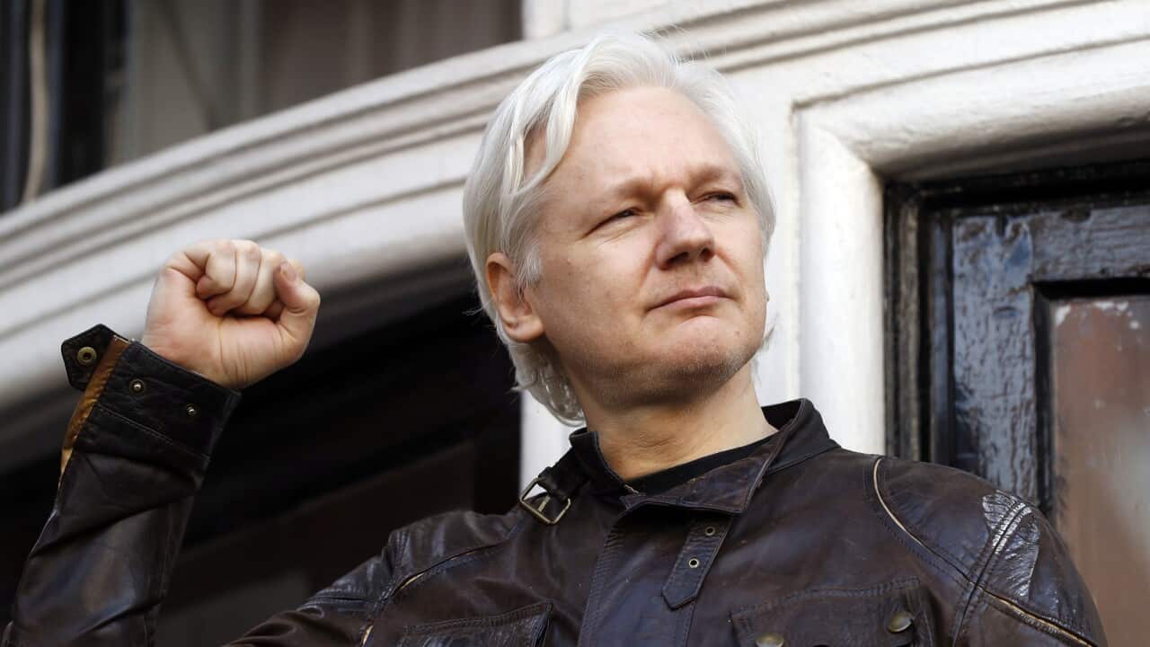 Julian Assange in front of a building. His fist is raised in the air.