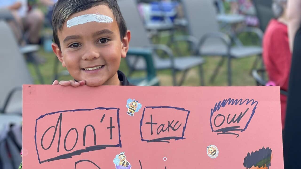 10-year-old Tai with brown hair and brown eyes holds a big red sign in front of him which says "Don't take our Pilliga". It is decorated with his drawings and bee stickers.