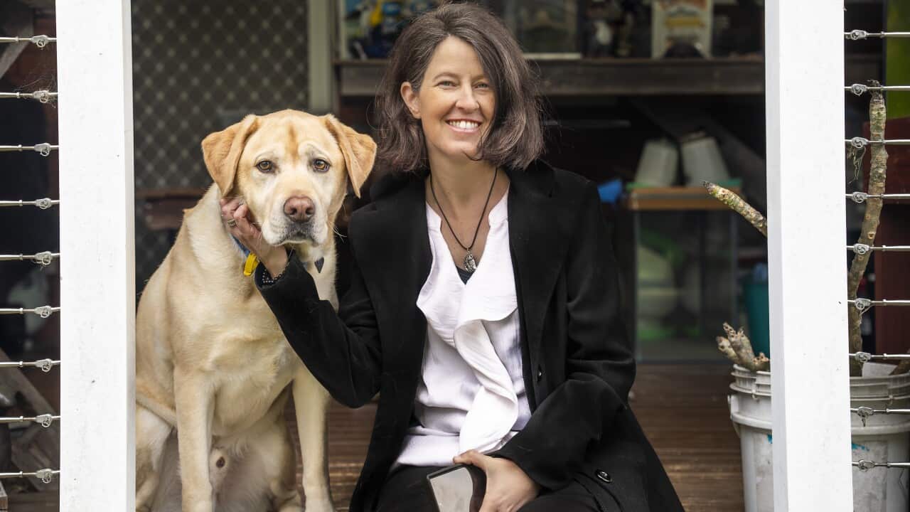A woman smiles at the camera while an assistance dog sits beside her.