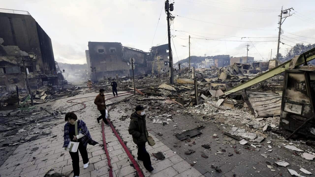 People walk past collapsed buildings following an earthquake in Wajima, Ishikawa prefecture, Japan