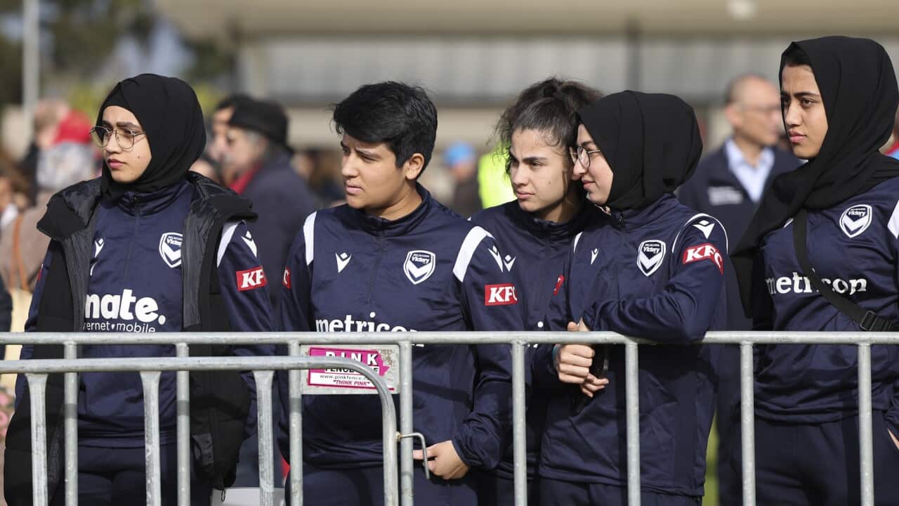 Five women in navy blue tracksuits. Four are wearing black hijabs.