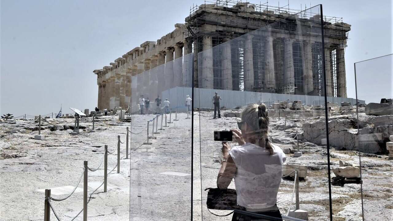 Tourists take photos behind plexiglass at the entrance of the Acropolis.