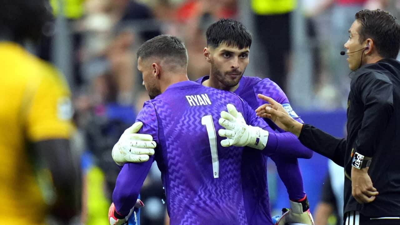 Two Socceroos goalkeepers embrace during a late goalkeeper substitution as a match official stands beside them on the touchline.