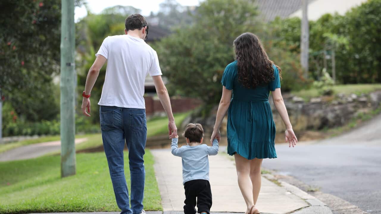 A child holds hands of a man and a woman who are walking by his side