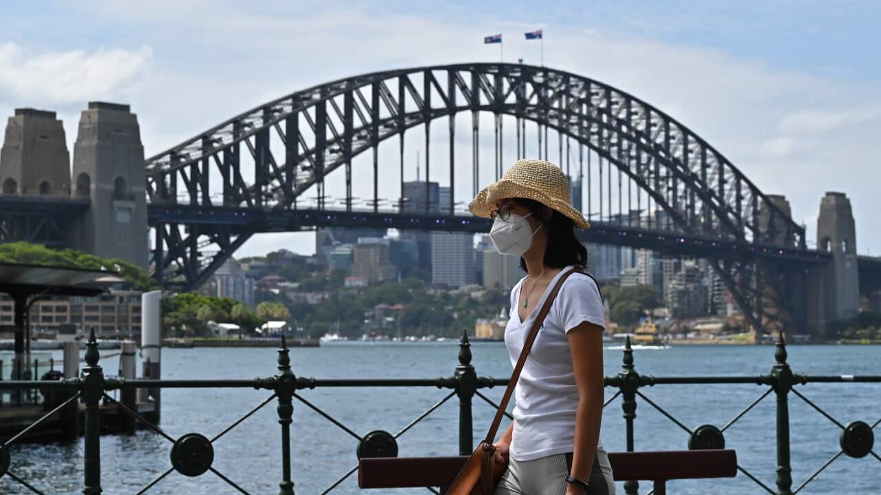 A woman wearing a hat and face mask walks past the Syndey Harbour Bridge