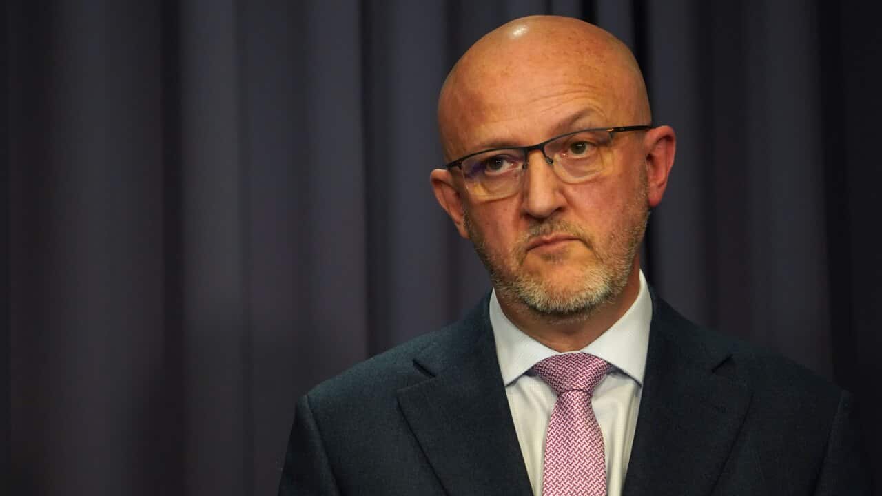 A man standing in front of a blue curtain.