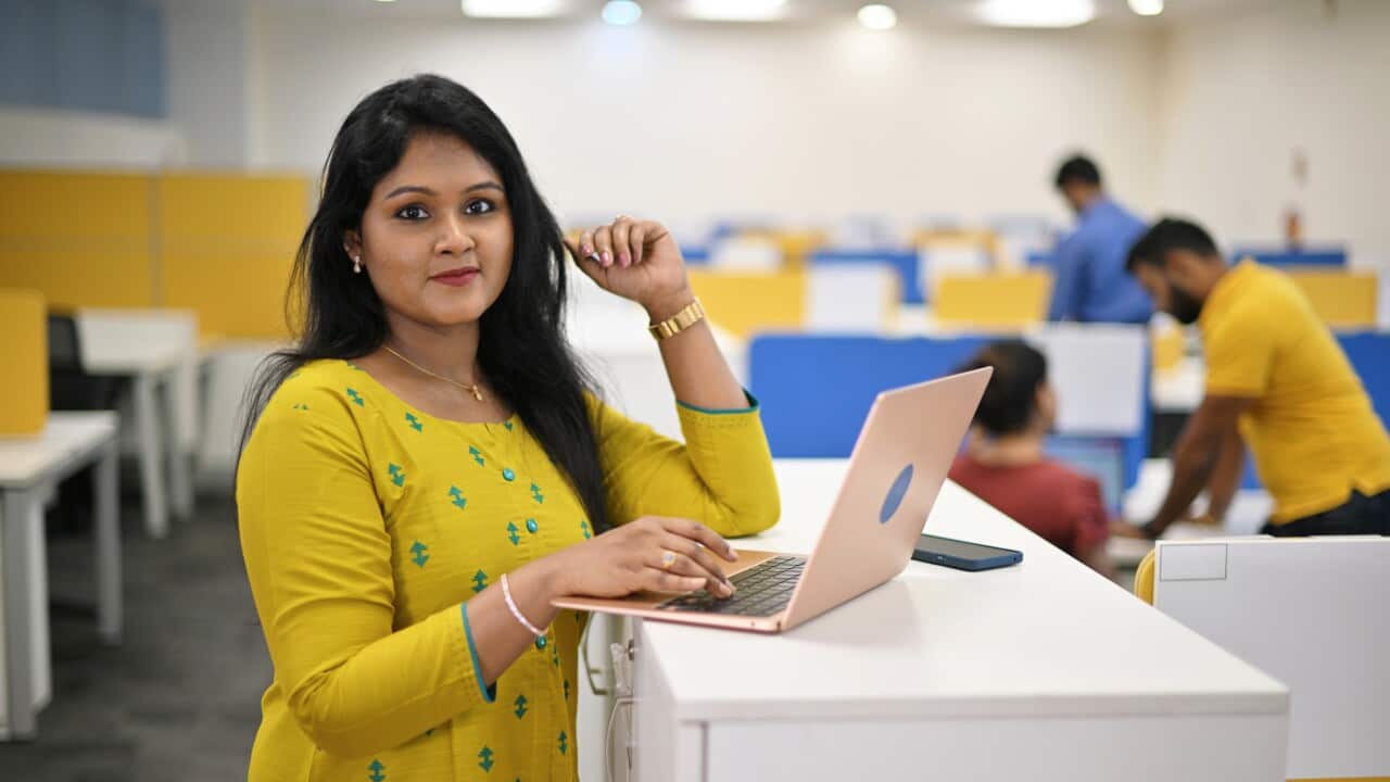 Mature woman looking at the camera while working on a laptop standing near her cubicle in an office