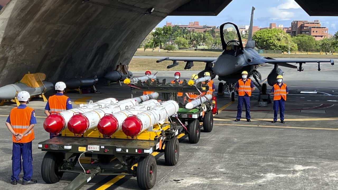 Military personnel stand next to weapons.