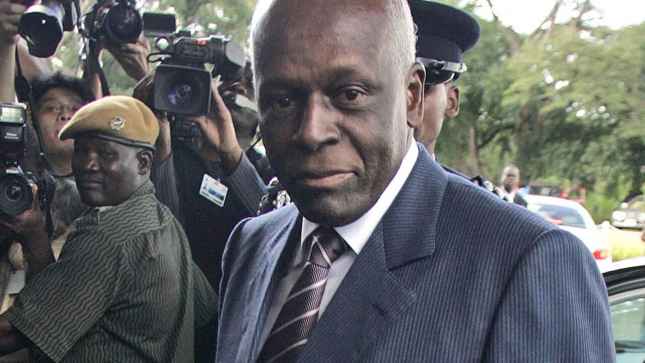 Former Angolan President José Eduardo Dos Santos, dressed in a navy blue suit, looks directly at the camera.